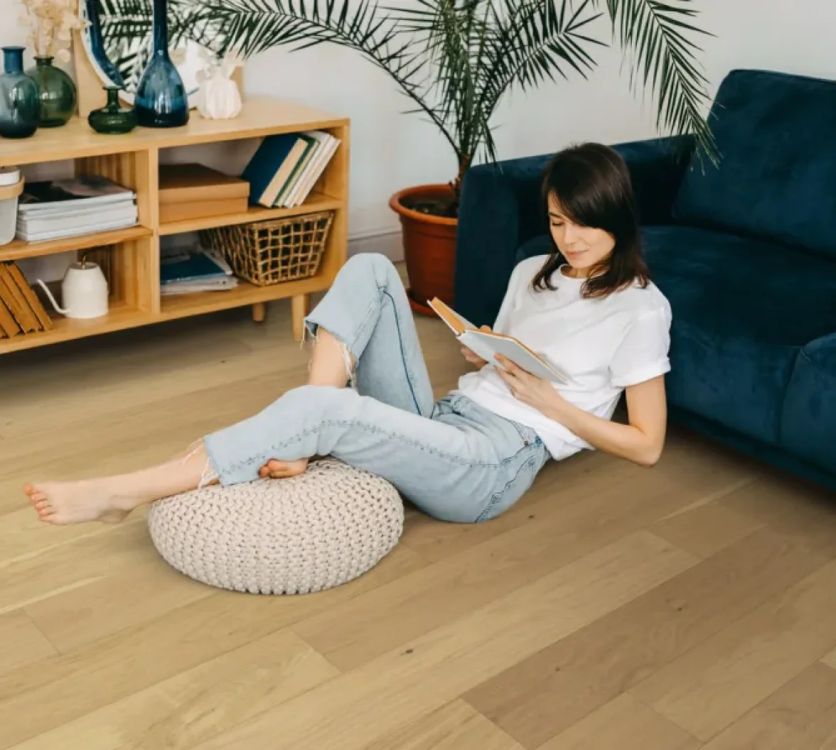 Woman sitting comfortably on natural hardwood floor reading a book