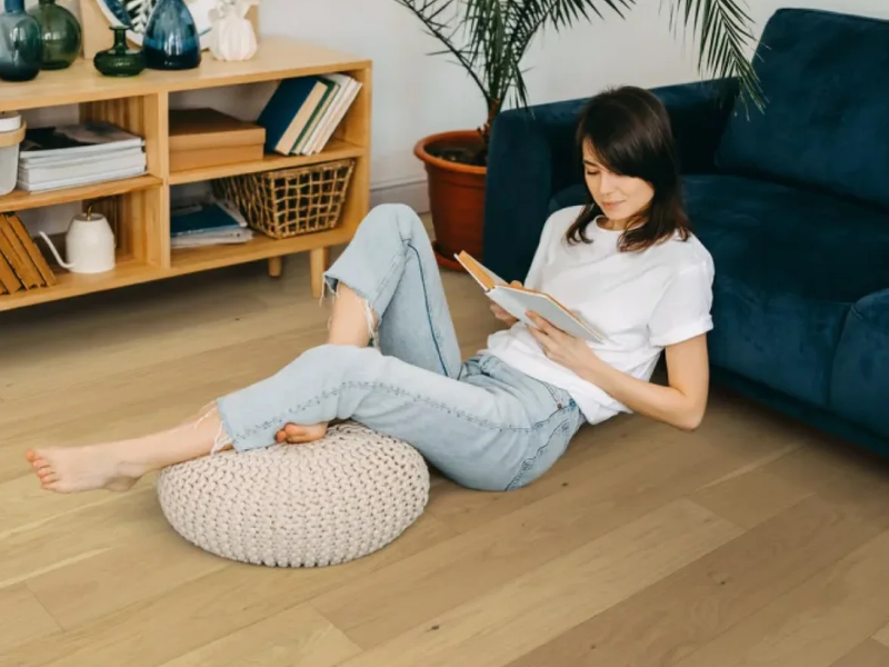 Woman sitting comfortably on natural hardwood floor reading a book